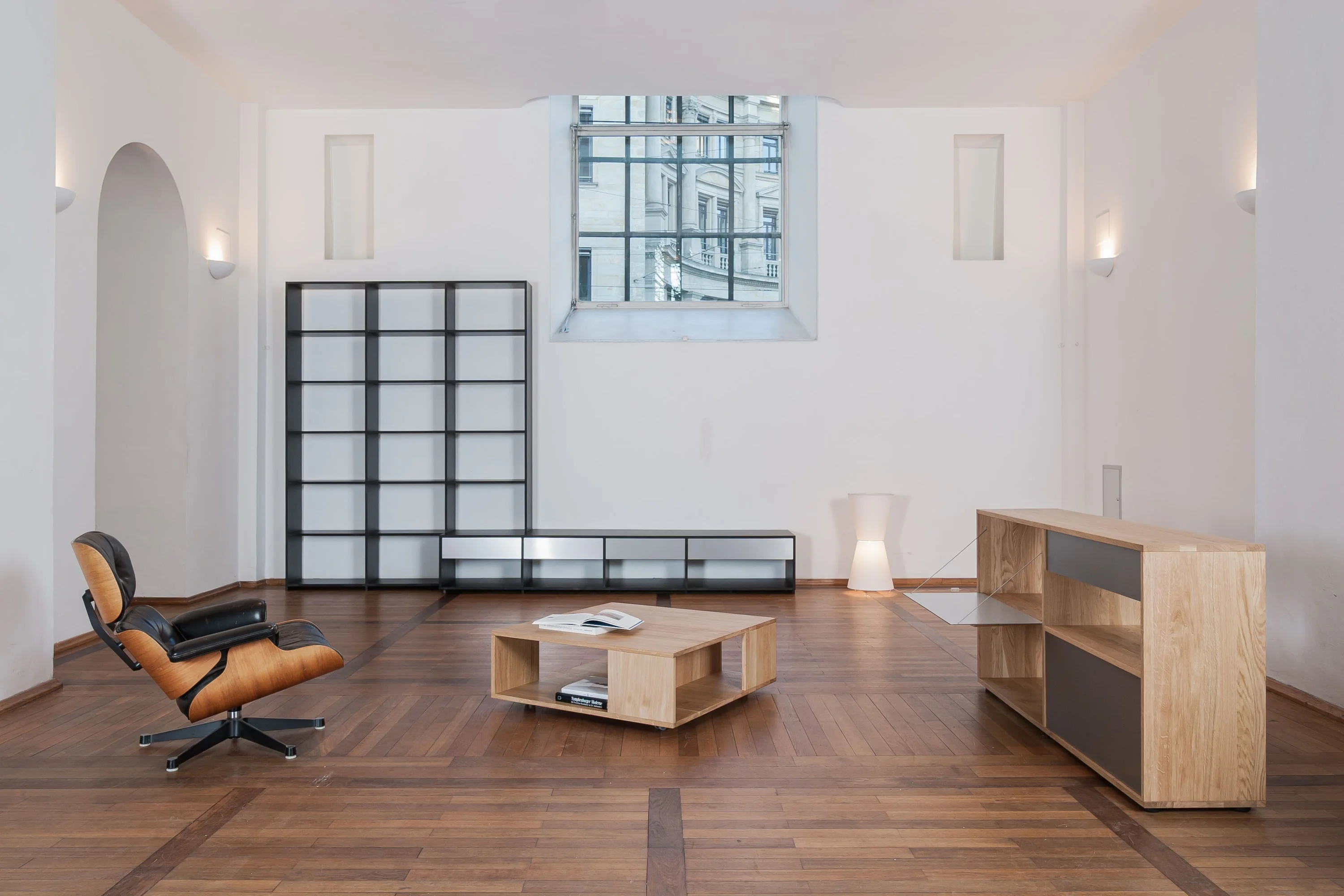 Hoher Raum mit Parkettboden, schwarzem Regal, Ledersessel, niedrigem Holztisch und Sideboard mit grauen Fronten.