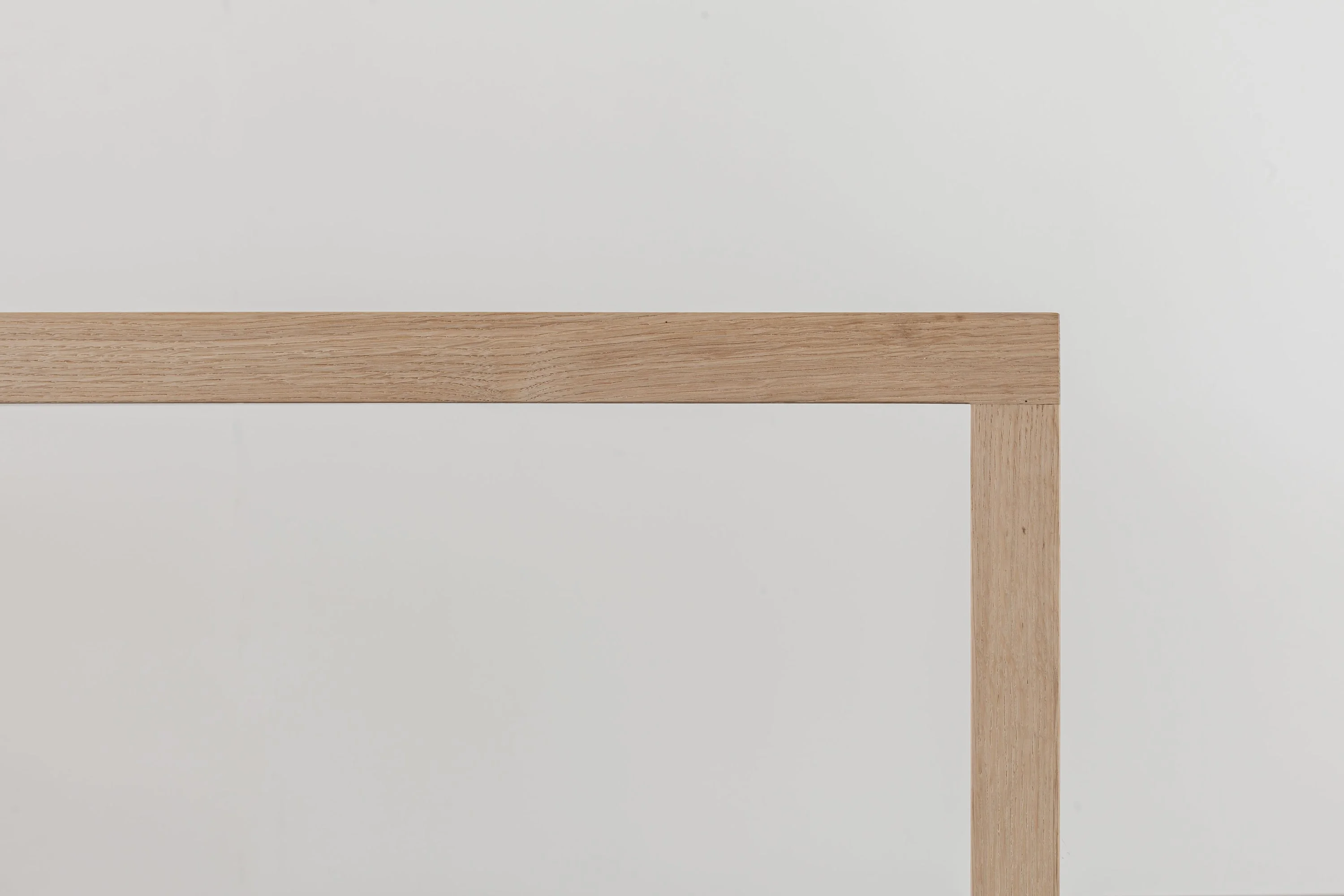 Ecke eines Holztisches mit schlankem Bein vor grauem Hintergrund.