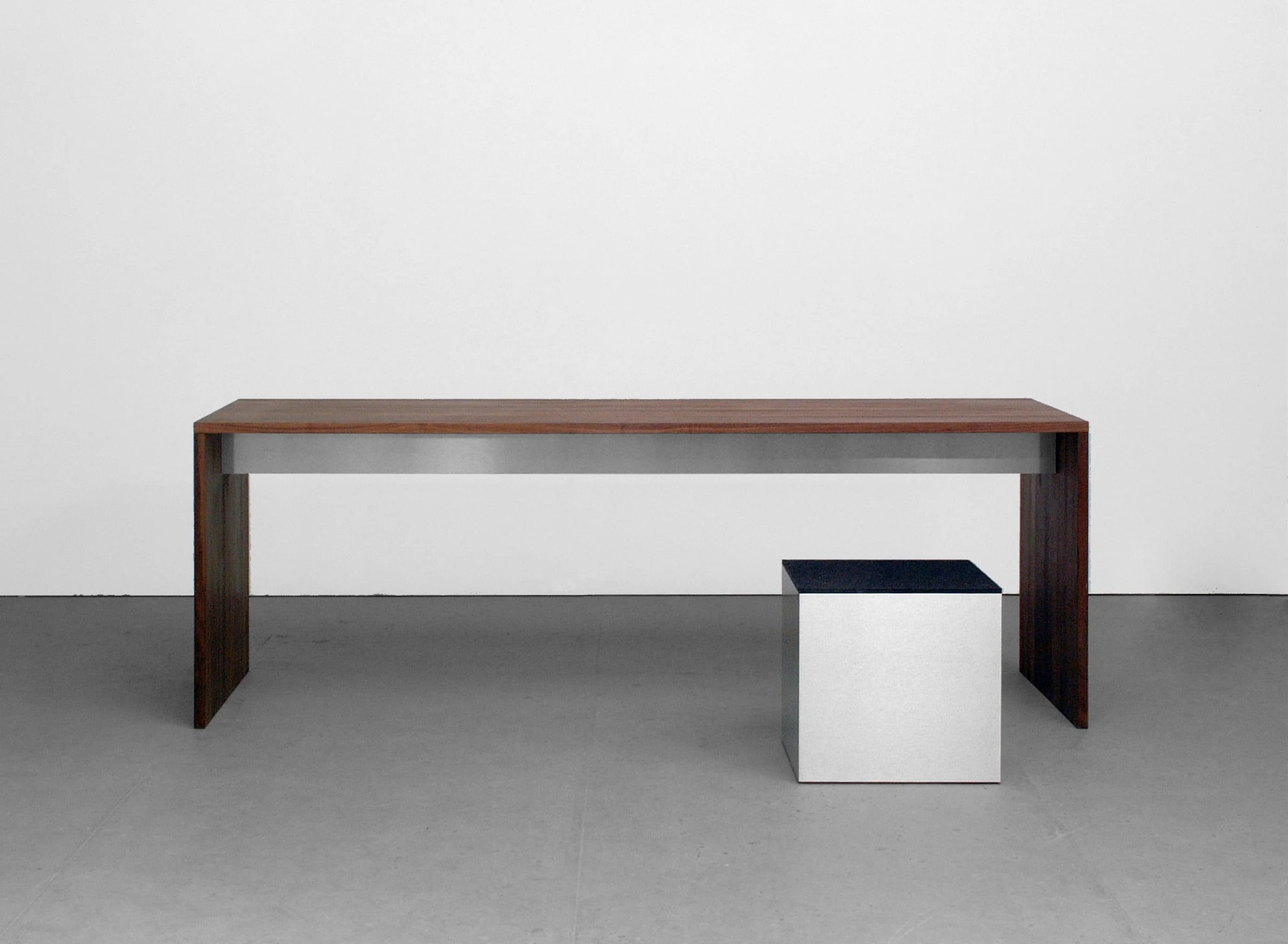 Tisch aus dunklem Holz mit Zarge aus Metall, daneben ein Kubus aus Metall.